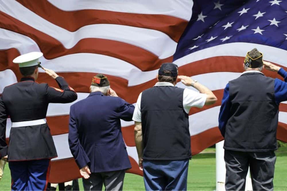 Veterans are saluting in front of the US flag