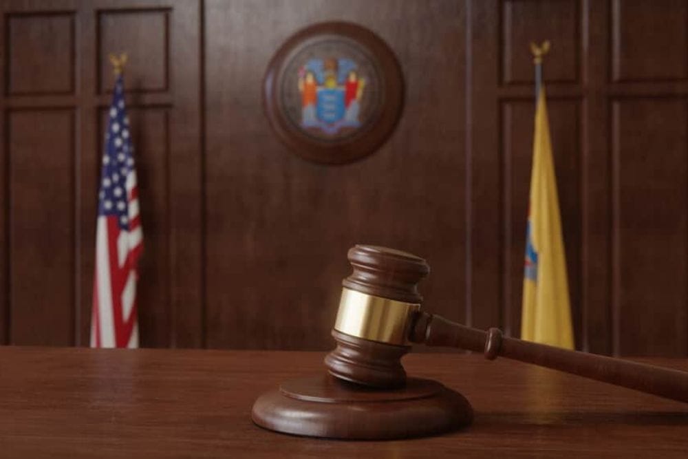 Courtroom scene with US flag and state seal and flag of the state of New Jersey.