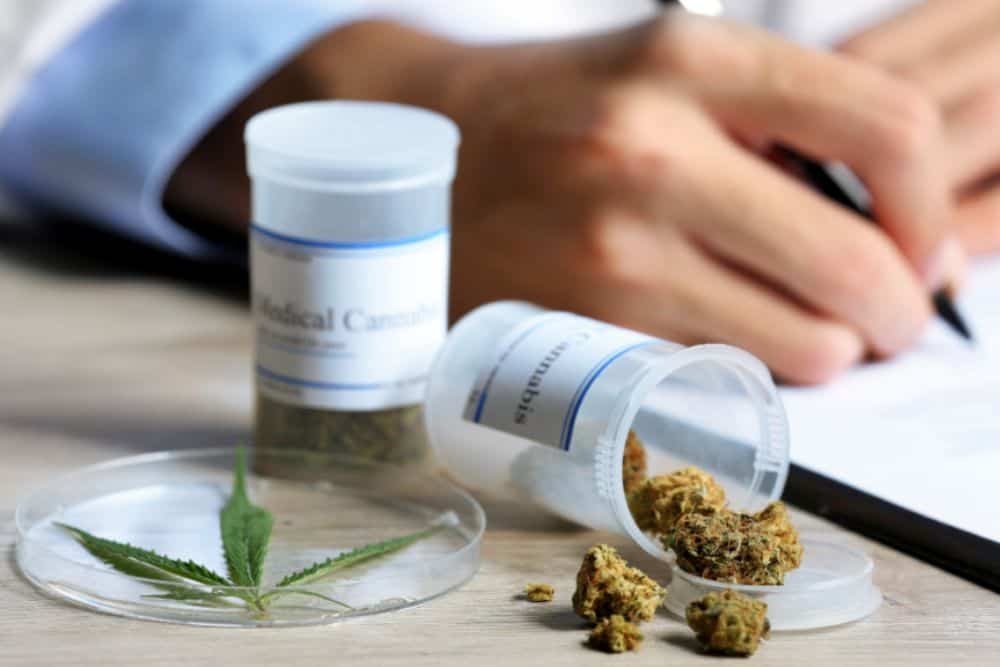 Doctor writing on prescription blank and bottle with medical cannabis on table.