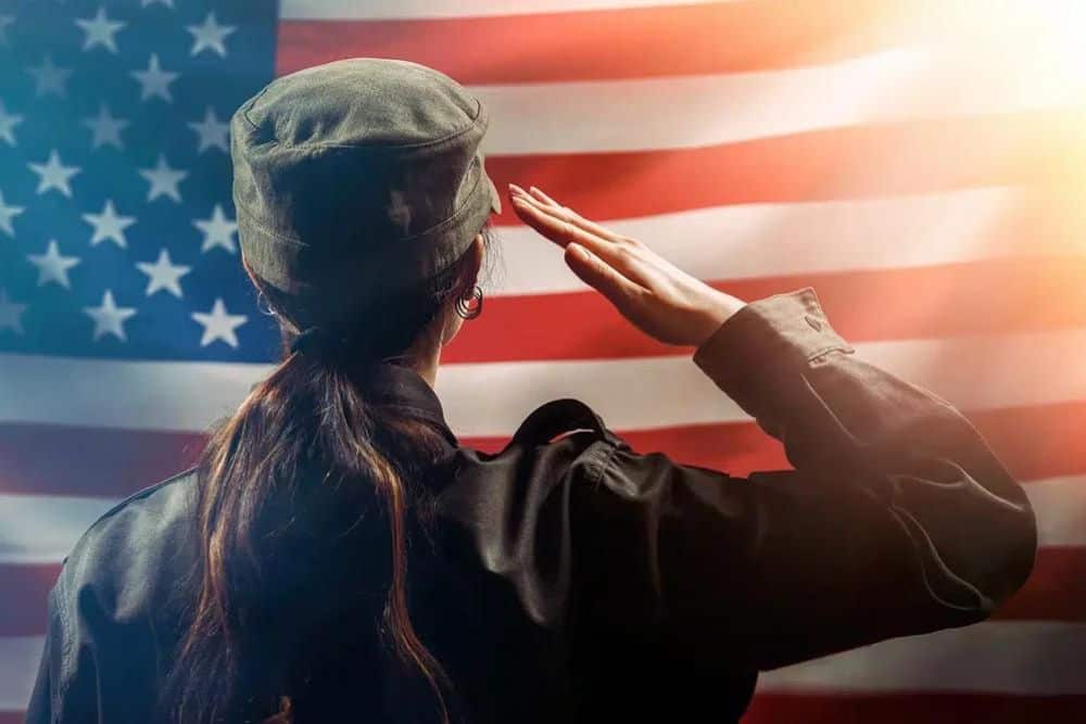 A female soldier salutes against the background of the American flag