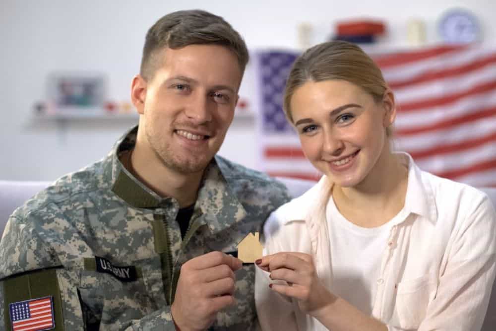 Smiling US male soldier and his wife showing wooden house sign