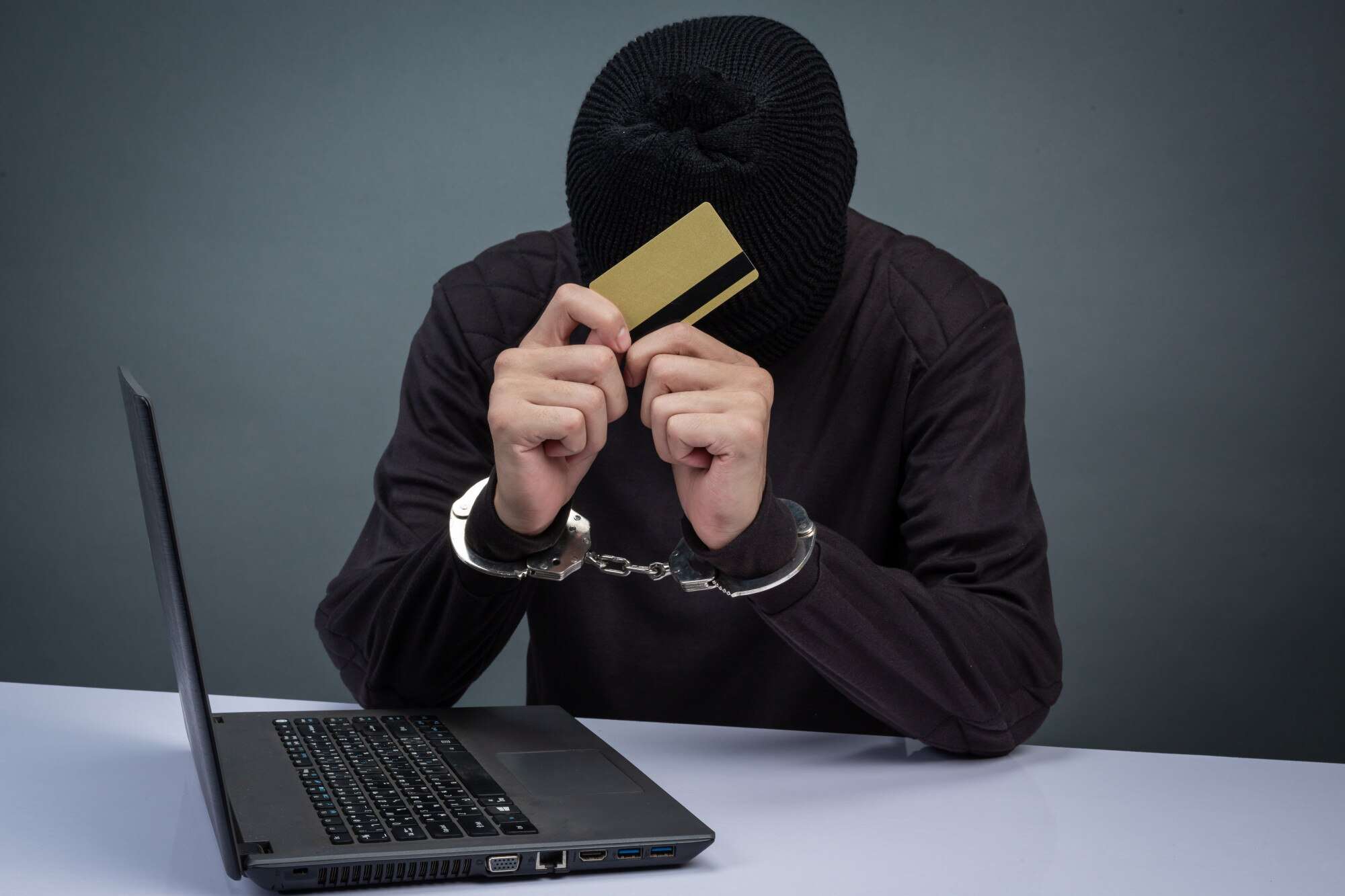 A cyber-thief in handcuffs and with credit card